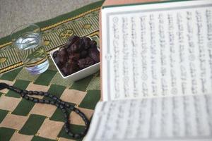 iftar-zeit getrocknete datteln heiliger koran glas wasser und tasbih auf betendem teppich oder sejadah foto