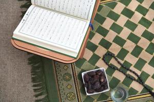 iftar-zeit getrocknete datteln heiliger koran glas wasser und tasbih auf betendem teppich oder sejadah foto