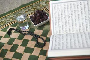 iftar-zeit getrocknete datteln heiliger koran glas wasser und tasbih auf betendem teppich oder sejadah foto