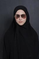 Junge muslimische Geschäftsfrau in traditioneller Kleidung oder Abaya und Sonnenbrille posiert vor schwarzer Tafel foto