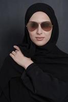 Junge muslimische Geschäftsfrau in traditioneller Kleidung oder Abaya und Sonnenbrille posiert vor schwarzer Tafel foto