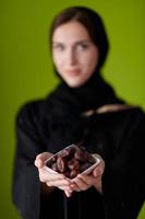 Frau in Abaya hält eine Dattelfrucht und ein Glas Wasser foto