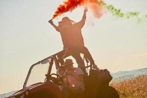 Aufgeregte Menschen, die Spaß daran haben, einen schönen sonnigen Tag mit bunten Fackeln zu genießen, während sie ein Offroad-Buggy-Auto fahren foto