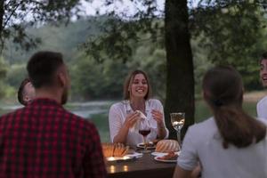 freunde, die rotweinglas toasten, während sie ein französisches picknick-abendessen im freien haben foto