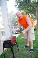 glücklicher Mann bereitet Würstchen auf dem Grill zu foto