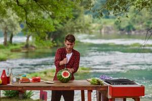 Mann schneidet saftige Wassermelone während einer französischen Dinnerparty im Freien foto