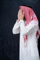 arabischer mann, der traditionelles beten zu gott macht, hält hände in betender geste vor schwarzer tafel foto