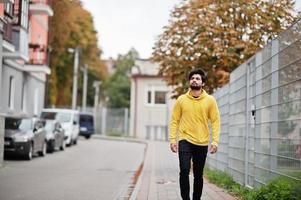 urbaner junger Hipster-Indianer in einem modischen gelben Sweatshirt. Cooler südasiatischer Typ trägt einen Hoodie, der auf der Herbststraße spazieren geht. foto