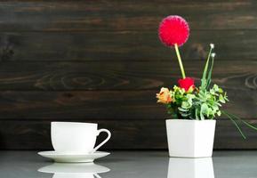 Kaffeetasse und Blumenstrauß aus künstlicher Blumenvase über dem Tisch foto