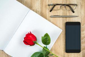 rote rosen auf leerem notizbuchtagebuch mit smartphone-valentinsgrußkonzept foto