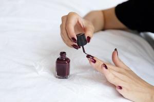 Nahaufnahme weiblicher Hände, die Nagellack in roter Farbe auf weißem Leinenbett, Mode- und Schönheitskonzept machen foto