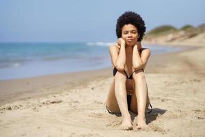 Schwarze Frau, die im Sommer am Sandstrand sitzt foto