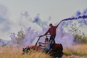 Aufgeregte Menschen, die Spaß daran haben, einen schönen sonnigen Tag mit bunten Fackeln zu genießen, während sie ein Offroad-Buggy-Auto fahren foto