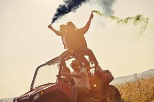 Aufgeregte Menschen, die Spaß daran haben, einen schönen sonnigen Tag mit bunten Fackeln zu genießen, während sie ein Offroad-Buggy-Auto fahren foto