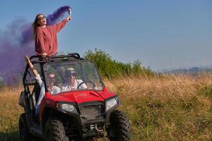 Aufgeregte Menschen, die Spaß daran haben, einen schönen sonnigen Tag mit bunten Fackeln zu genießen, während sie ein Offroad-Buggy-Auto fahren foto