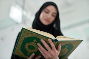 Porträt einer jungen muslimischen Frau, die den Koran in einem modernen Zuhause liest foto