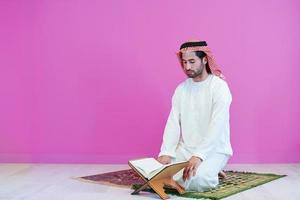 junger arabischer muslimischer mann, der zu hause den koran liest foto