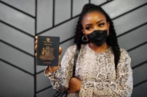 afroamerikanerin mit schwarzer gesichtsmaske zeigt grenada-pass in der hand. coronavirus in amerika land, grenzschließung und quarantäne, virusausbruchskonzept. foto