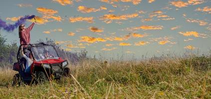 Aufgeregte Menschen, die Spaß daran haben, einen schönen sonnigen Tag mit bunten Fackeln zu genießen, während sie ein Offroad-Buggy-Auto fahren foto