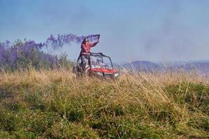 Aufgeregte Menschen, die Spaß daran haben, einen schönen sonnigen Tag mit bunten Fackeln zu genießen, während sie ein Offroad-Buggy-Auto fahren foto