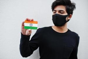 asiatischer mann trägt ganz schwarz mit gesichtsmaske und hält in der hand die indische flagge isoliert auf weißem hintergrund. Coronavirus-Länderkonzept. foto