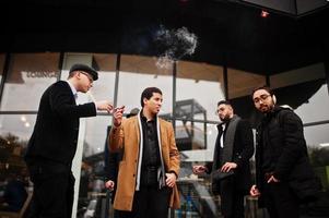 Gruppe hübscher, gut gekleideter Gangster im Retro-Stil, die im Freien rauchen. multiethnische männliche Junggesellen-Mafia-Party. foto