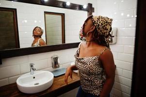Schöne afroamerikanische Frau mit Dreadlocks im Leopardenoutfit, die im WC-Café in den Spiegel schaut. schönes cooles modisches schwarzes junges mädchen drinnen. foto