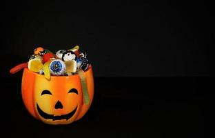 orangefarbener Kürbis-Kürbislaternentopf voller verschiedener Süßigkeiten. traditionelle Halloween-Pralinen und Geleewürmer. schwarzer hintergrund mit kopienraum. Süßes oder Saures-Konzept. foto