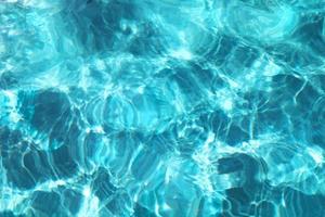 Türkisblau gewellte Wasseroberfläche des Schwimmbades. sommerferien-resort-konzept. hintergrund der wasserkräuselung unter hellem sonnigem himmel. foto