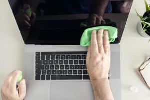 computerreinigungskonzept. Draufsicht auf eine männliche menschliche Hand, die einen Laptop-Bildschirm mit Reinigungsspray und antistatischem Tuch reinigt foto