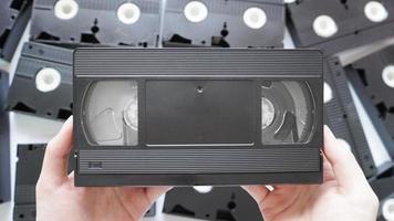 hände, die eine vhs-bandrückseite mit verstreuten bändern im hintergrund halten. foto