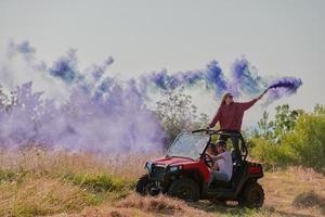 Aufgeregte Menschen, die Spaß daran haben, einen schönen sonnigen Tag mit bunten Fackeln zu genießen, während sie ein Offroad-Buggy-Auto fahren foto