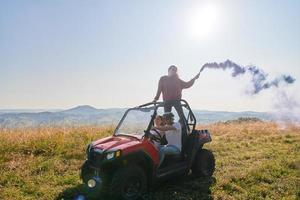 Aufgeregte Menschen, die Spaß daran haben, einen schönen sonnigen Tag mit bunten Fackeln zu genießen, während sie ein Offroad-Buggy-Auto fahren foto