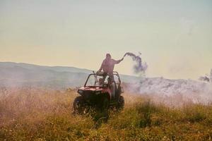 Aufgeregte Menschen, die Spaß daran haben, einen schönen sonnigen Tag mit bunten Fackeln zu genießen, während sie ein Offroad-Buggy-Auto fahren foto