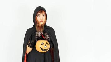 Schönes Mädchen mit schwarzen und orangefarbenen Haaren in schwarzem Kleid und Hexenhut hält Kürbis. Halloween-Konzept. foto