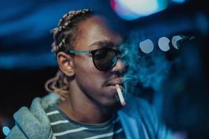 Afrikanischer Mann, der eine Zigarre raucht, im Hintergrund die Lichter der Stadt foto