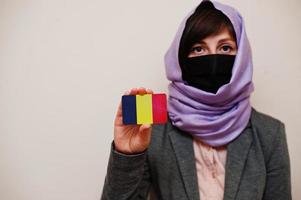 porträt einer jungen muslimischen frau, die formelle kleidung trägt, gesichtsmaske und hijab-kopftuch schützt, tschad-flaggenkarte vor isoliertem hintergrund hält. Coronavirus-Länderkonzept. foto