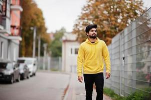 urbaner junger Hipster-Indianer in einem modischen gelben Sweatshirt. Cooler südasiatischer Typ trägt einen Hoodie, der auf der Herbststraße spazieren geht. foto