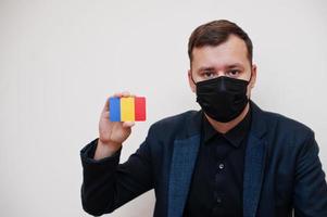 europäischer mann trägt schwarze formelle und schützt gesichtsmaske, hält rumänische flaggenkarte isoliert auf weißem hintergrund. europa coronavirus covid country konzept. foto