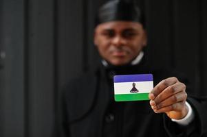 Afrikanischer Mann trägt schwarzen Durag und hält die Lesotho-Flagge zur Hand, isoliert auf dunklem Hintergrund. foto