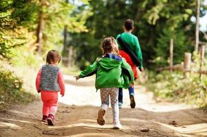 Rücken von drei Kindern, die auf Holzbergen spazieren gehen. Familienreisen und Wandern mit Kindern.