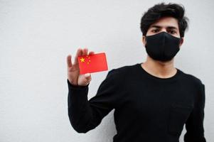 asiatischer mann trägt ganz schwarz mit gesichtsmaske und hält china-flagge in der hand isoliert auf weißem hintergrund. Coronavirus-Länderkonzept. foto
