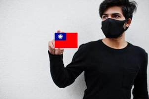 asiatischer mann trägt ganz schwarz mit gesichtsmaske und hält taiwan-flagge in der hand isoliert auf weißem hintergrund. Coronavirus-Länderkonzept. foto