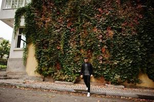 porträt des stilvollen arabischen bartmannes trägt einen grauen rollkragenpullover und eine schwarze jaket. arabischer vorbildlicher kerl auf einem hintergrund von herbstblättern. foto