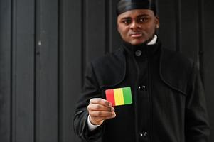 Afrikanischer Mann trägt schwarzen Durag, hält die guinea-Flagge zur Hand, isoliert auf dunklem Hintergrund. foto