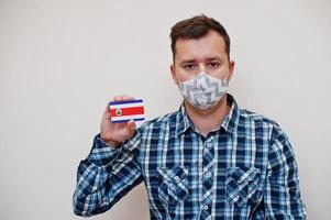 mann im karierten hemd zeigt costa rica-flaggenkarte in der hand, trägt schutzmaske isoliert auf weißem hintergrund. Coronavirus-Konzept der amerikanischen Länder. foto