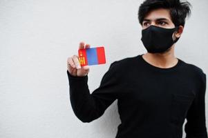 asiatischer mann trägt ganz schwarz mit gesichtsmaske und hält die mongolei-flagge in der hand isoliert auf weißem hintergrund. Coronavirus-Länderkonzept. foto