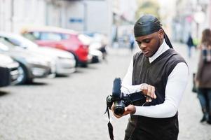 junger professioneller afroamerikanischer videofilmer mit professioneller kamera mit professioneller ausrüstung. Afro-Kameramann mit schwarzem Duraq, der Videos macht. foto