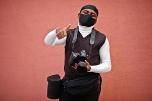 junger professioneller afroamerikanischer videofilmer mit professioneller kamera mit professioneller ausrüstung. afro-kameramann mit schwarzem duraq und gesichtsschutzmaske, der ein video macht. foto