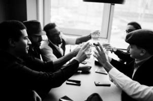 Eine Gruppe hübscher, gut gekleideter Gangster im Retro-Stil verbringt Zeit im Club, sitzt und trinkt Whiskey. multiethnische männliche Junggesellen-Mafia-Party im Restaurant. foto